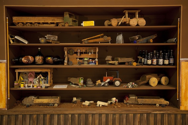 Esta é a vitrine do armazém de brinquedos, que traz carrinhos feitos por crianças. Tudo que está aí foi construído com restos de objetos cotidianos encontrados em seus quintais. No dia a dia, elas inventam e se divertem assim.